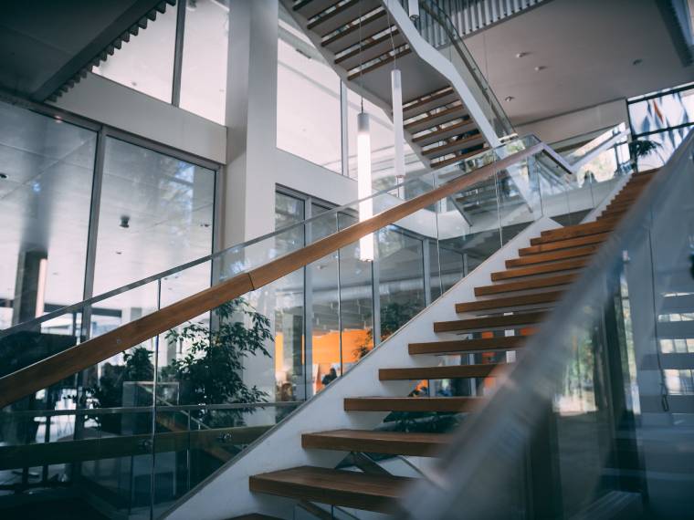 Schody z drewnianymi trepami i nowoczesną, szklaną balustradą